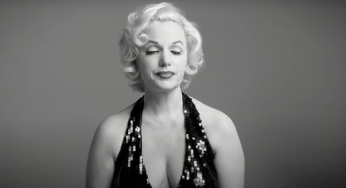 Black and white photo of a blonde Marilyn Monroe lookalike wearing a disdainful expression and dark, sequined gown with a deep plunge neckline